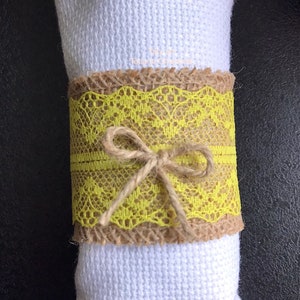 May include: A yellow lace napkin ring with a burlap base and a brown twine bow.