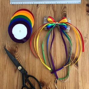 Puede incluir: Suministros de artesanía sobre una superficie de madera. Incluye cintas de colores del arcoíris, un lazo decorativo, tijeras y una regla. El lazo es de arpillera y encaje, con cintas coloridas. El texto "Taty art Tetiana Chankrob" es visible.