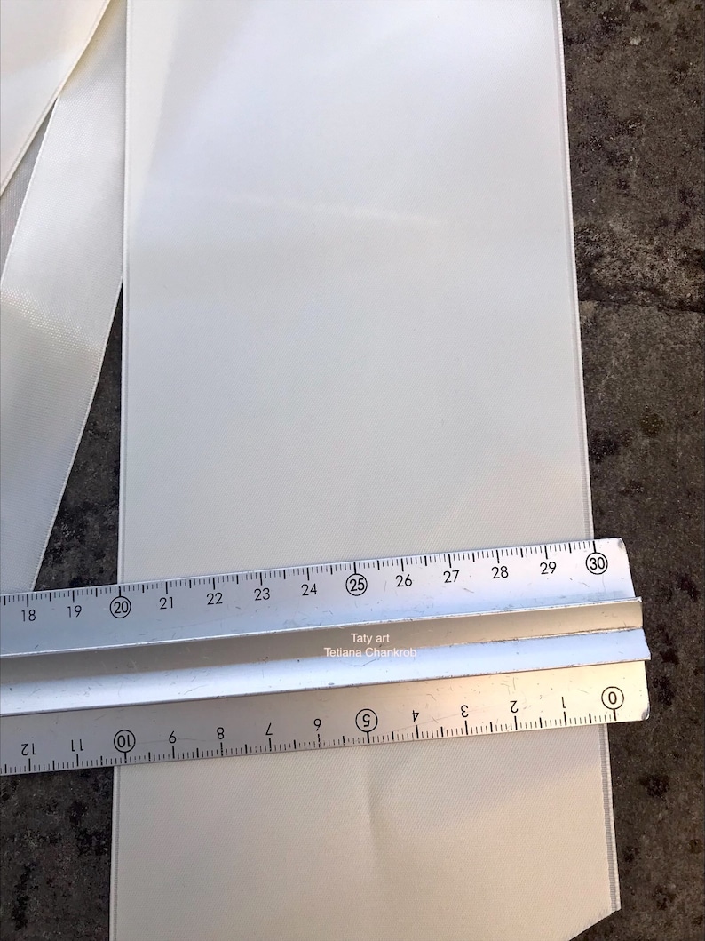 Op de afbeelding: Een close-up van een witte stof met een liniaal die de lengte meet. De liniaal toont metingen van 0 tot 30 cm, met de tekst "Taty art Tetiana Chankrob" zichtbaar. De stof lijkt een licht, getextureerd materiaal te zijn.