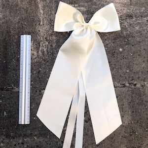 May include: A large ivory satin bow with long tails. The bow is tied in a classic style with a center loop and two long tails.