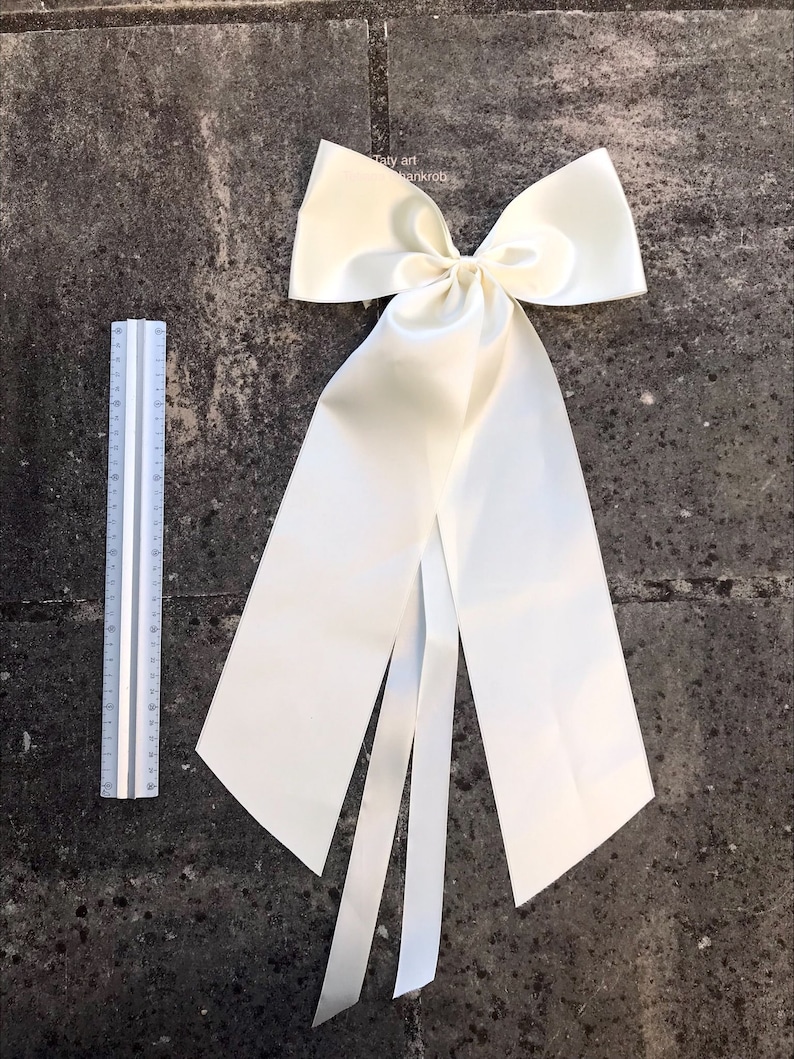 May include: A large ivory satin bow with long tails. The bow is tied in a classic style with a center loop and two long tails.