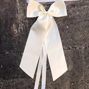 May include: A large ivory satin bow with long tails. The bow is tied with a single knot in the center and has a smooth, silky texture.