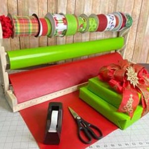 Puede incluir: Una estaci&oacute;n de envoltura de regalos de madera con un soporte de cinta integrado, un soporte de rollo de papel y una gu&iacute;a de corte. La estaci&oacute;n contiene rollos de papel de regalo, cinta y un dispensador de cinta adhesiva. Tambi&eacute;n hay tijeras y una caja de regalo envuelta con un lazo.