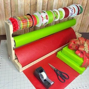 Puede incluir: Un soporte de madera para envolver regalos con dos rollos de papel de regalo, uno rojo y uno verde, y una variedad de carretes de cinta. El soporte tambi&eacute;n incluye un dispensador de cinta adhesiva y unas tijeras.
