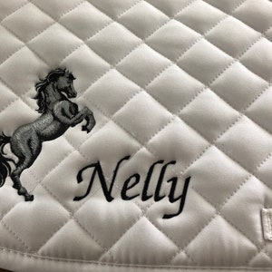 May include: White quilted saddle pad with a black embroidered horse and the name "Nelly" in cursive.