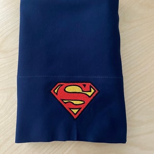 May include: A dark blue pillowcase with an embroidered Superman logo in red and yellow.