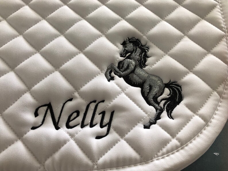 May include: White quilted saddle pad with black embroidery of a horse and the name "Nelly".