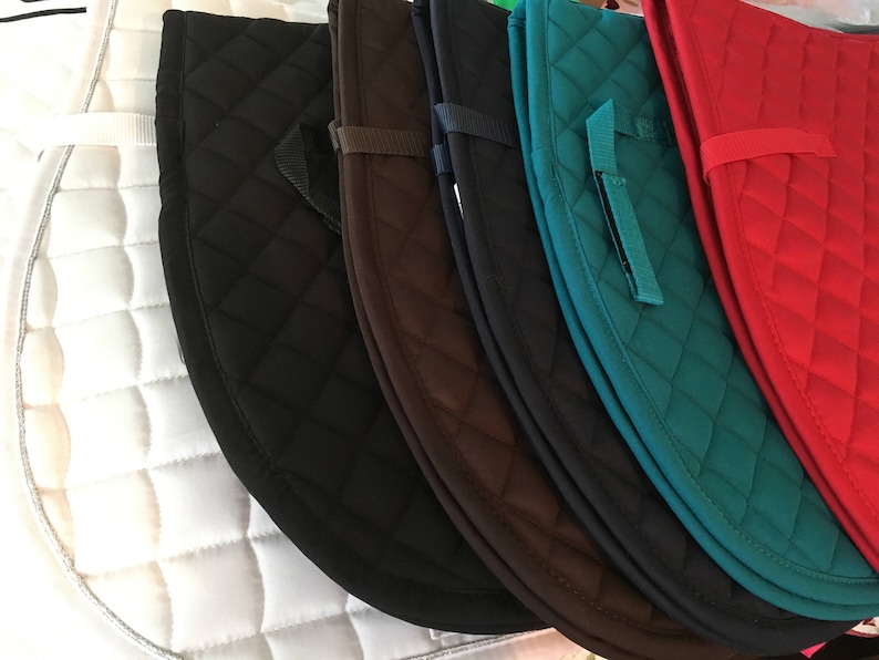 May include: A set of six quilted saddle pads in various colours, including white, black, brown, teal, navy, and red. The pads are made of a soft, quilted material and have a diamond pattern.