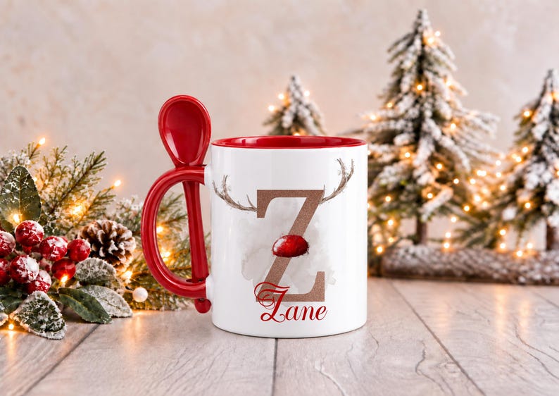 May include: A white ceramic mug with a red interior and a matching red spoon integrated into the handle. The front features a large brown letter Z with reindeer antlers and a red nose, with the name Zane printed in red script below.