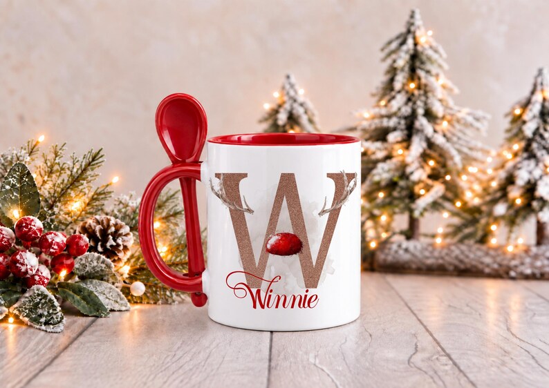 May include: A white ceramic mug with a red interior and a matching red spoon integrated into the handle. The front features a large, glittery copper letter W decorated with reindeer antlers and a red nose, with the name Winnie written below.