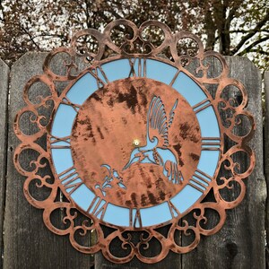 May include: A copper-colored metal clock with a blue face and a hummingbird design. The clock is surrounded by a decorative metal frame.