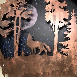 Op de afbeelding: Een koperkleurig metalen zaagblad met een uitgesneden ontwerp van een wolf die huilt naar de maan in een bossetting. De achtergrond is donkerblauw met witte sterren.