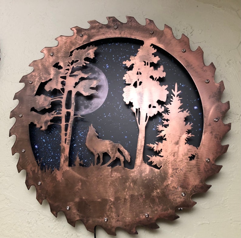 Op de afbeelding: Een koperkleurige cirkelzaagblad met een silhouet van een wolf, bomen en een volle maan tegen een achtergrond van een sterrenhemel.