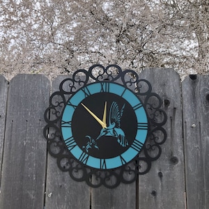May include: A black metal clock with a blue face and Roman numerals. A gold hummingbird silhouette is on the face of the clock.