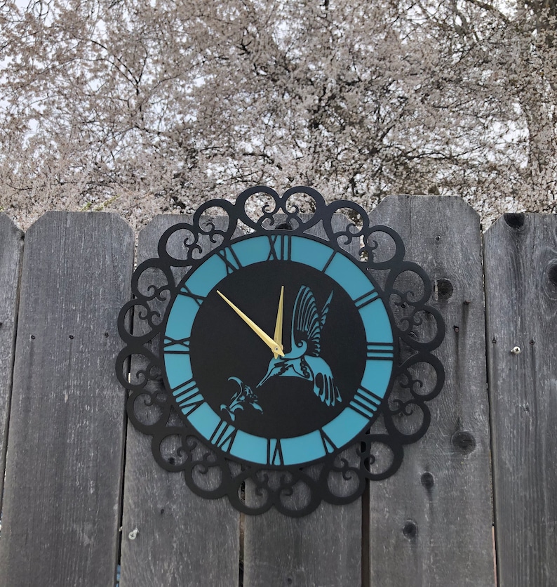 May include: A black metal clock with a blue face and Roman numerals. A gold hummingbird silhouette is on the face of the clock.