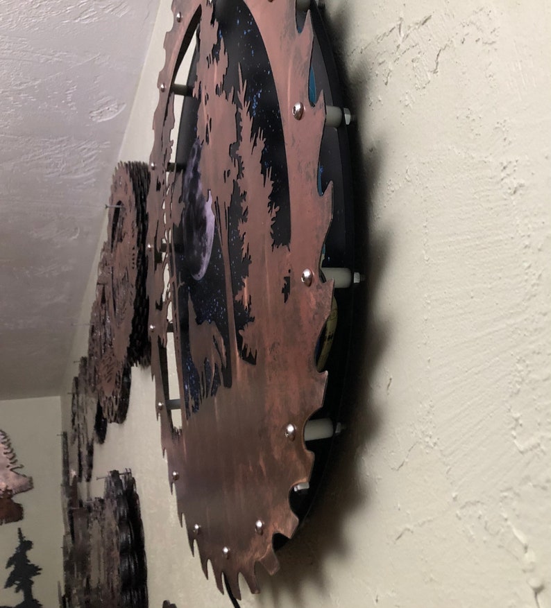 Op de afbeelding: Een cirkelvormig metalen wandkunstwerk met een rustieke bruine afwerking. De kunst toont een silhouet van een boom met een volle maan en sterren op de achtergrond. Het metaal is getextureerd en heeft een verweerde uitstraling.