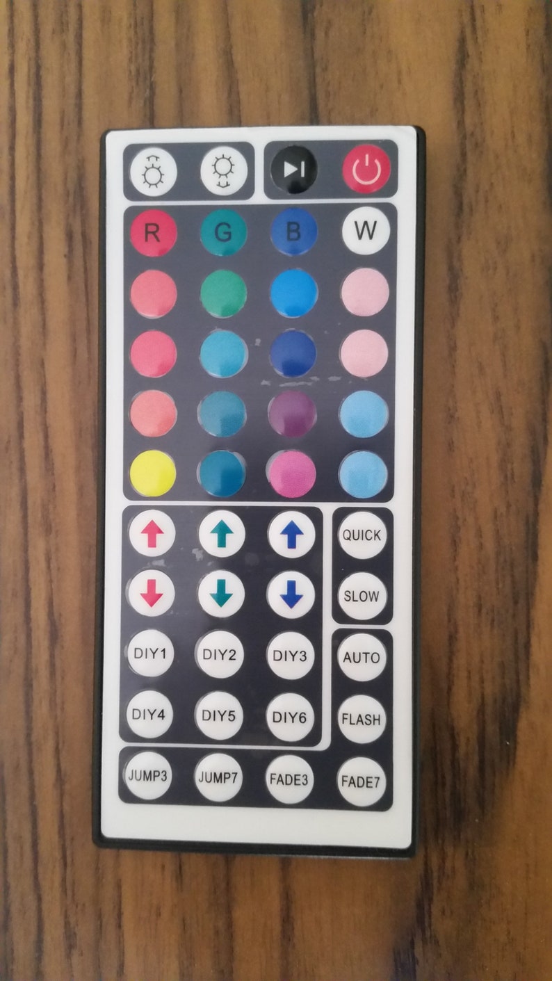 Op de afbeelding: Een zwarte afstandsbediening met witte knoppen voor het bedienen van LED-verlichting. De knoppen omvatten kleurkeuzes, snelheidsinstellingen en functies zoals "snel", "langzaam", "automatisch", "flits", "sprong" en "fade".