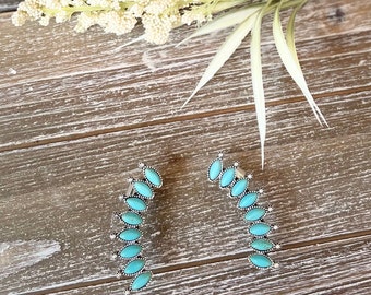 May include: A pair of turquoise and silver ear cuffs. Each cuff features a curved design with multiple turquoise stones.