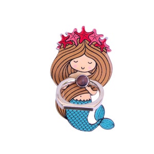 May include: A phone ring holder featuring a cartoon mermaid with brown hair, a blue tail, and a crown of red starfish. The ring is gold and has a clear gem in the center.