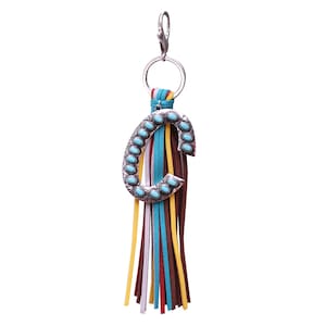 May include: A silver charm with the letter "C" decorated with turquoise stones and a multi-colored tassel keychain.