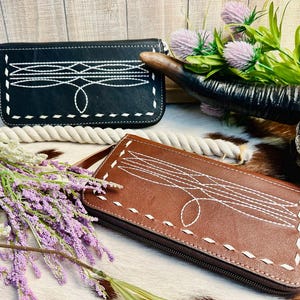 May include: Two leather wallets with white stitching and a geometric design. The wallet on the left is black and the wallet on the right is brown.