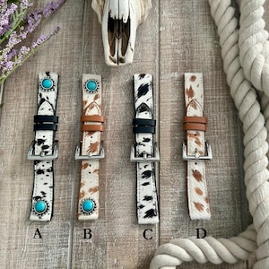 May include: Four different watch bands with a cowhide pattern. The bands are black, brown, white and black, and white and brown. Each band has a turquoise stone accent.