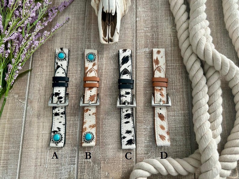 May include: Four different watch bands with a cowhide pattern. The bands are black, brown, white and black, and white and brown. Each band has a turquoise stone accent.