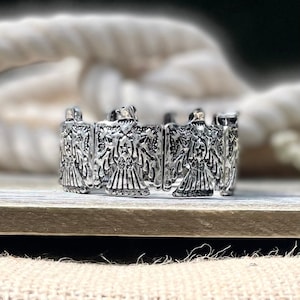 Könnte beinhalten: Silberarmband mit einem sich wiederholenden Muster aus stilisierten Adlermotiven. Das Armband ist aus Metall und hat eine polierte Oberfläche.