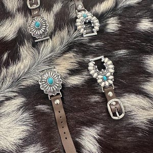 May include: Four brown leather watch bands with silver and turquoise embellishments. The bands feature different designs, including a horseshoe, a flower, and a sun.