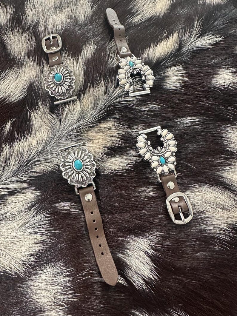 May include: Four brown leather watch bands with silver and turquoise embellishments. The bands feature different designs, including a horseshoe, a flower, and a sun.