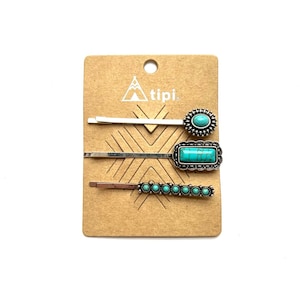 Peut inclure: Ensemble de trois pinces à cheveux argentées avec des pierres turquoise. Les pinces sont sur une carte brune avec le mot "atipi." imprimé dessus.