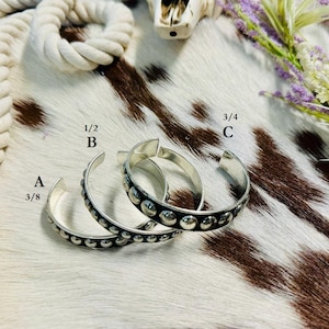 May include: Three silver bracelets with a textured design of small circles. The bracelets are labeled A, B, and C with their respective sizes: 3/8, 1/2, and 3/4.