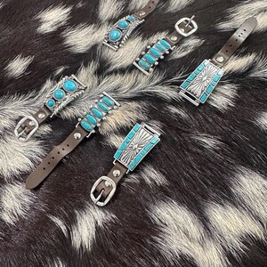 May include: Five different watch bands with turquoise stones and silver accents. The bands are made of brown leather and have a buckle closure.