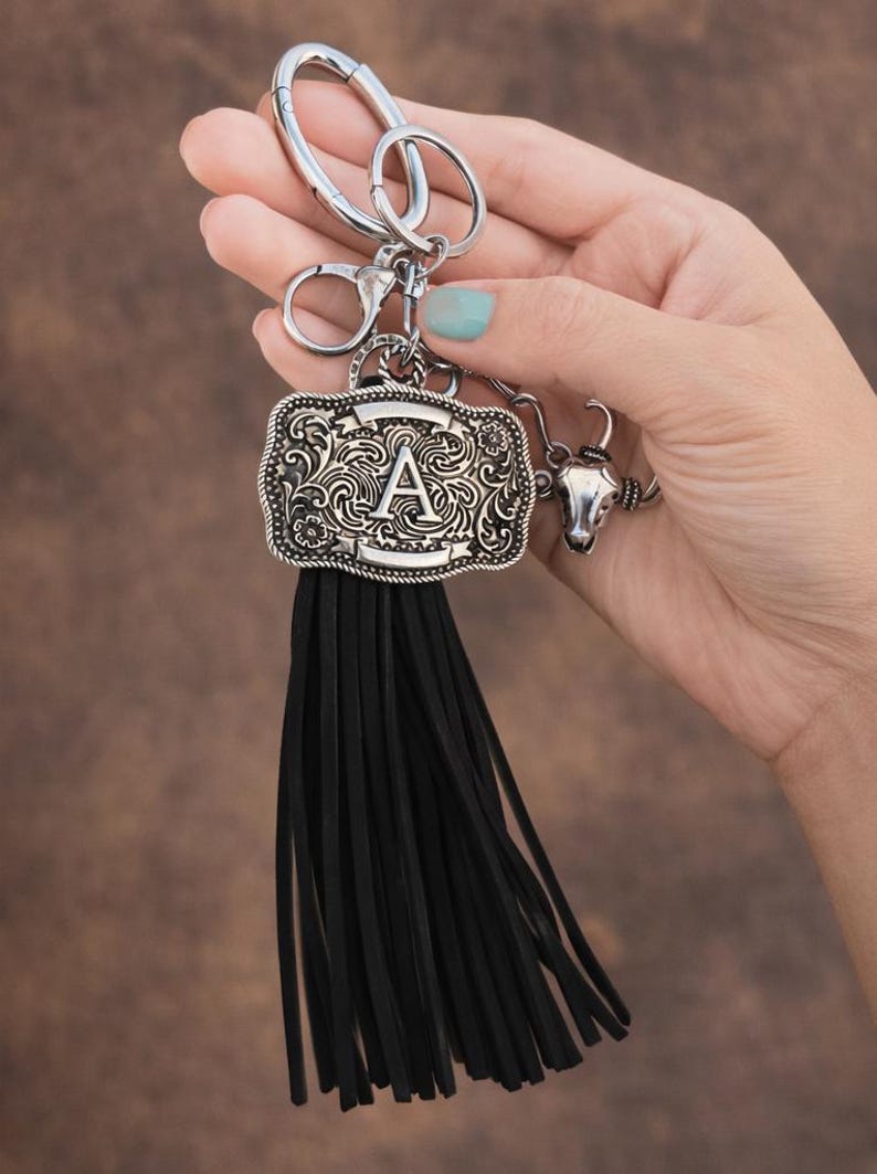 May include: Silver-tone keychain with a decorative buckle featuring the letter "A" and a black tassel. The keychain also includes a small bull head charm, perfect for adding a touch of Western flair to your keys or bag.