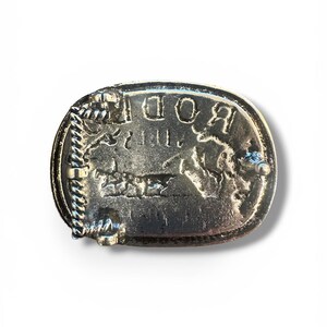 May include: Silver-toned metal belt buckle with the word "ROD" in raised letters. The buckle has a rectangular shape with rounded edges and a rope-like border. A detailed image of a horse is visible.