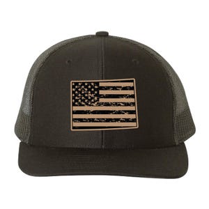 May include: A dark olive green trucker hat with a distressed tan American flag patch. The hat features a mesh back and a curved brim. The flag design includes stars and stripes.