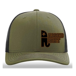 May include: Olive green and black trucker hat with the text "RAISED RIGHT" in brown. The hat features a star and an elephant graphic. The hat has a mesh back and a curved brim.