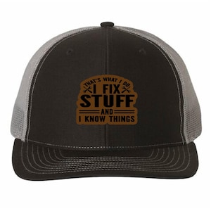 Peut inclure: Casquette de camionneur noire avec un dos en filet gris et une visière incurvée. Le devant arbore un écusson marron avec le texte "THAT'S WHAT I DO, I FIX STUFF, AND I KNOW THINGS". Fermeture réglable.