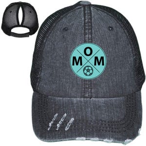 May include: Distressed black baseball cap with a mesh back and a ponytail opening. The front features a teal circle with the word "MOM" and a soccer ball graphic.