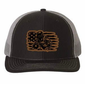May include: A black and grey trucker hat with a brown silhouette of a welder in front of an American flag.