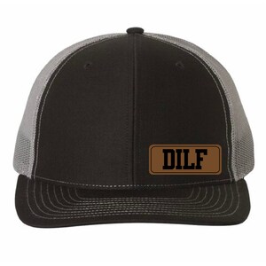 May include: A black and gray trucker hat with a brown leather patch that says "DILF" in black letters.
