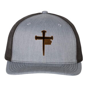 May include: Gray trucker hat with a brown cross design. The cross has the text "3 NAILS 1 CROSS 4 GIVEN". The hat has a gray front panel, a gray brim, and a black mesh back.