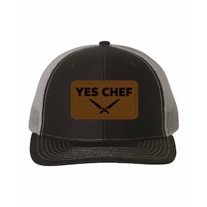 May include: A black and gray trucker hat with a brown patch that says "YES CHEF" with a pair of crossed knives.