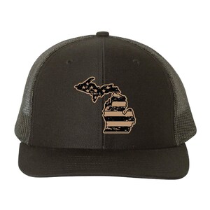 Peut inclure: Casquette de camionneur gris foncé avec un motif beige et noir de l'État du Michigan. Le motif ressemble au drapeau américain. La casquette a un dos en filet et une visière incurvée.