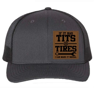 May include: A dark gray trucker hat with a black mesh back. The front features a brown square patch with the text "IF IT HAS TITS OR TIRES I CAN MAKE IT SQUEAL" in white.