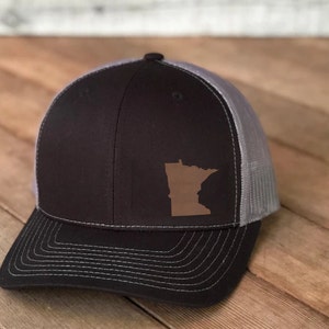 May include: A black and gray trucker hat with a brown outline of the state of Minnesota on the front.