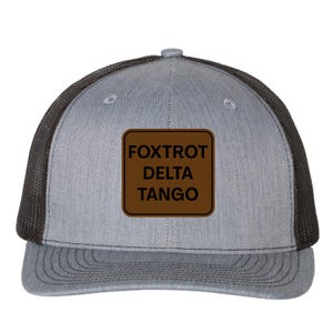 May include: Grey trucker cap with a black mesh back and a brown square patch. The patch displays the words "Foxtrot Delta Tango" in a bold font. The cap has a curved peak and a snap closure at the back.