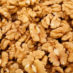 May include: A close-up image of a pile of walnut halves. The walnuts are light brown in colour and have a slightly wrinkled texture.