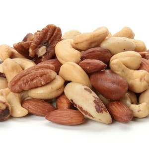 Puede incluir: Una mezcla de frutos secos que incluye almendras, anacardos, pacanas y nueces de Brasil. Los frutos secos son de color marrón claro y están dispuestos en un montón sobre un fondo blanco.