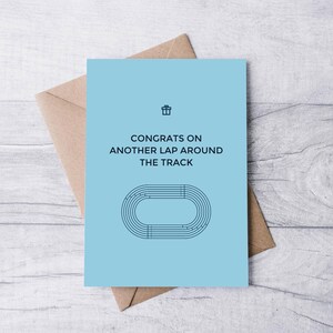 May include: A light blue greeting card with a running track design and the text "Congrats on another lap around the track".
